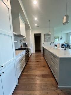 A long kitchen with white cabinets and hardwood floors.