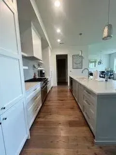 Modern kitchen with white cabinets, wooden floor, and a large island.