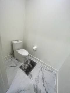 A bathroom with a toilet and a marble floor.
