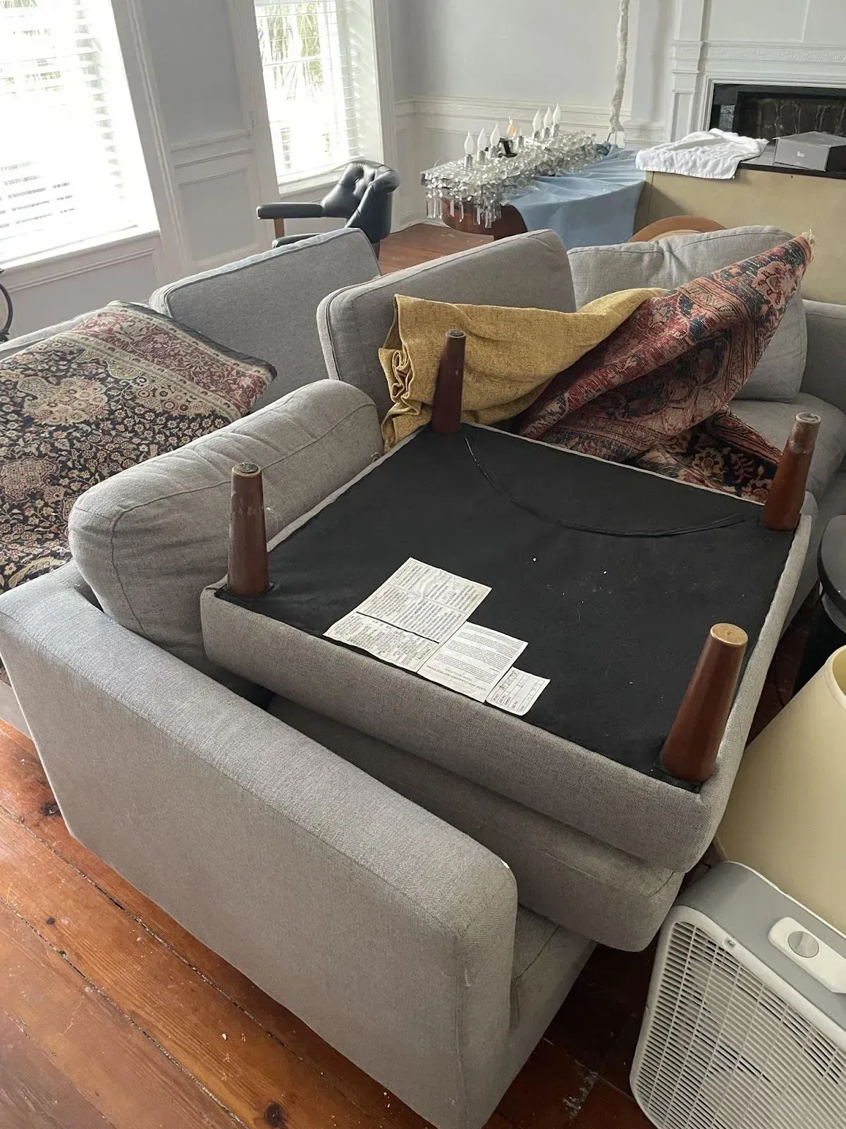 A gray sofa is partially flipped over, showing the underside with wooden legs and tags.