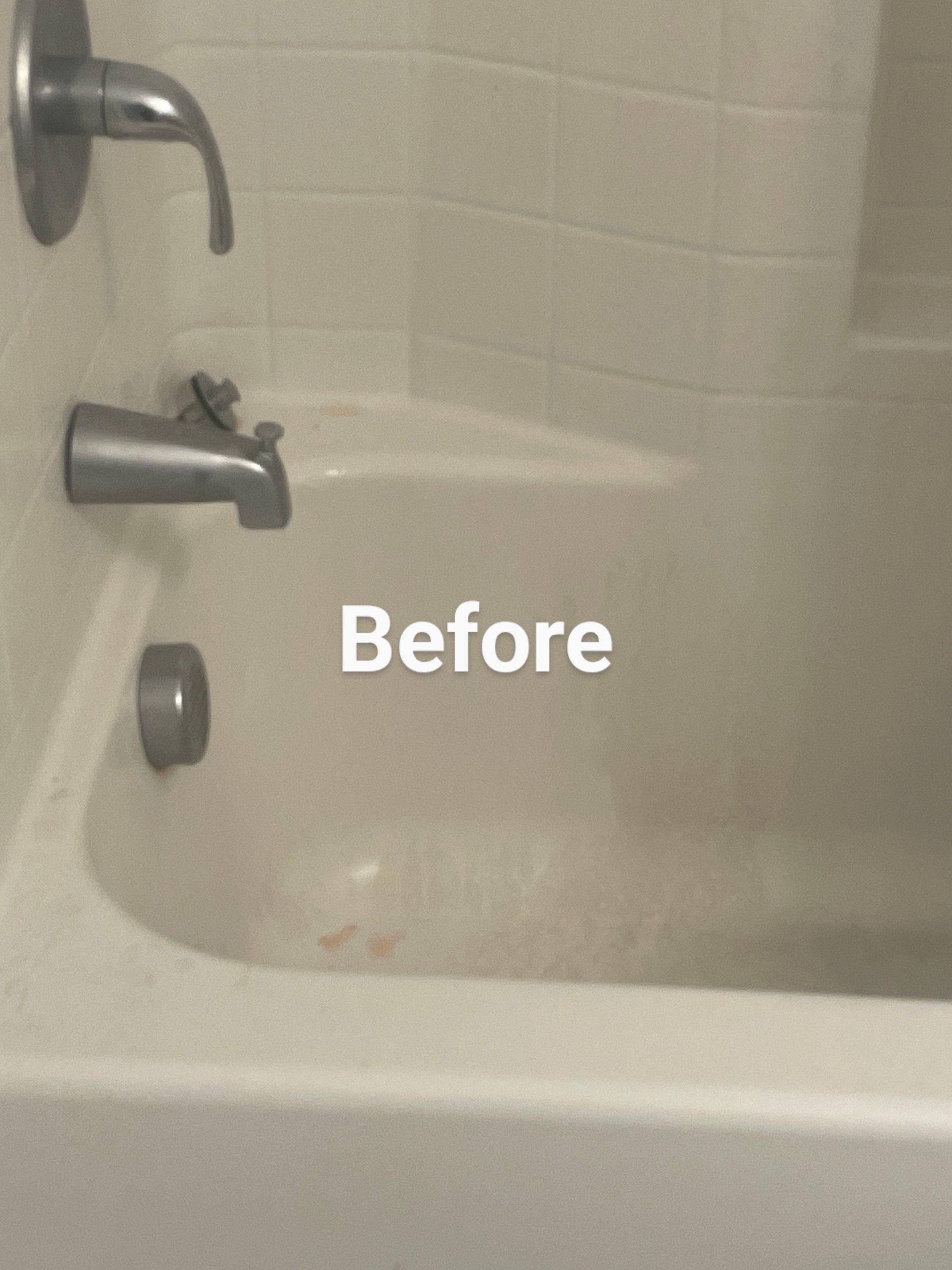 Bathtub with visible stains, before cleaning. Faucet visible, white tile wall.