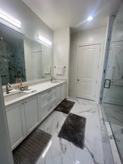 A bathroom with two sinks , a mirror and a walk in shower.