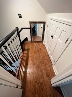 A hallway with hardwood floors and a mirror on the wall.