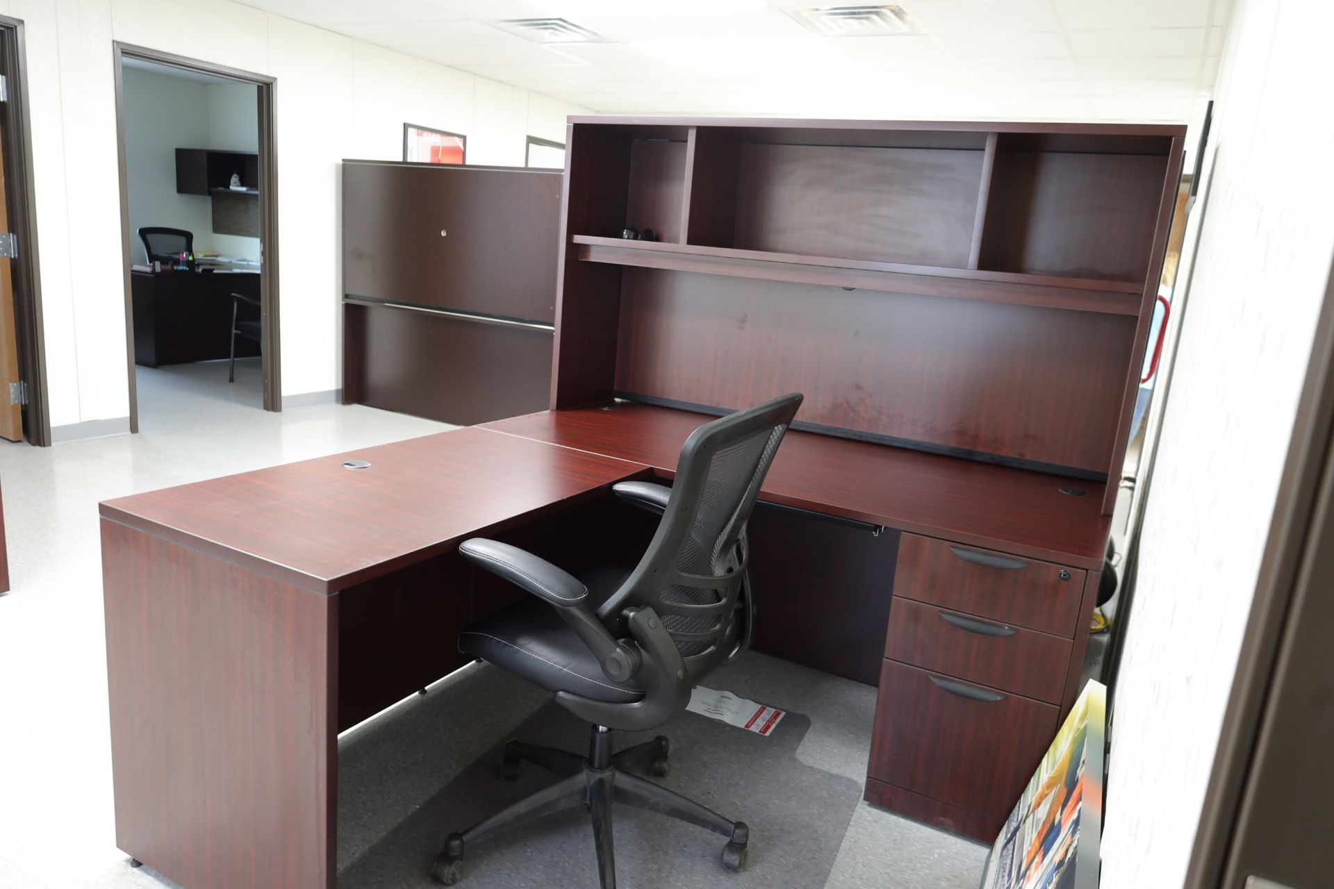 An office with a dark brown L-shaped desk, a black office chair, and a large shelving unit.