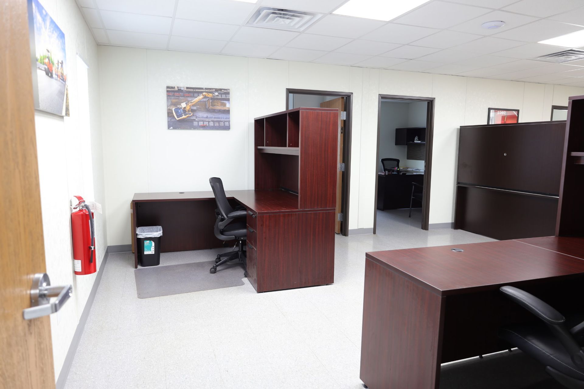 An empty office with desks, chairs, and doors. Fire extinguisher on the wall.