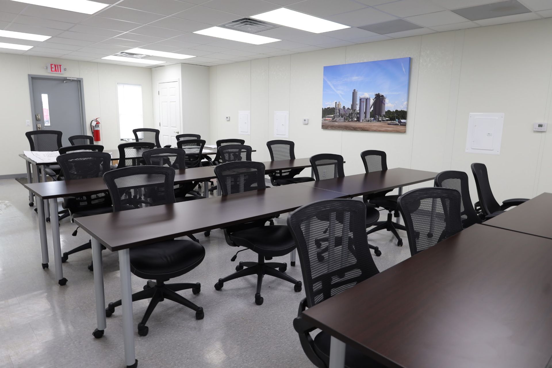 Empty classroom with rows of desks and black rolling chairs. A city skyline art hangs on the wall.