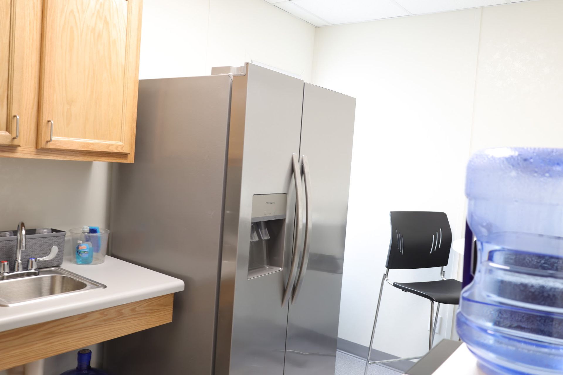 Kitchen with a stainless steel refrigerator, cabinets, sink, water cooler, and a black chair.