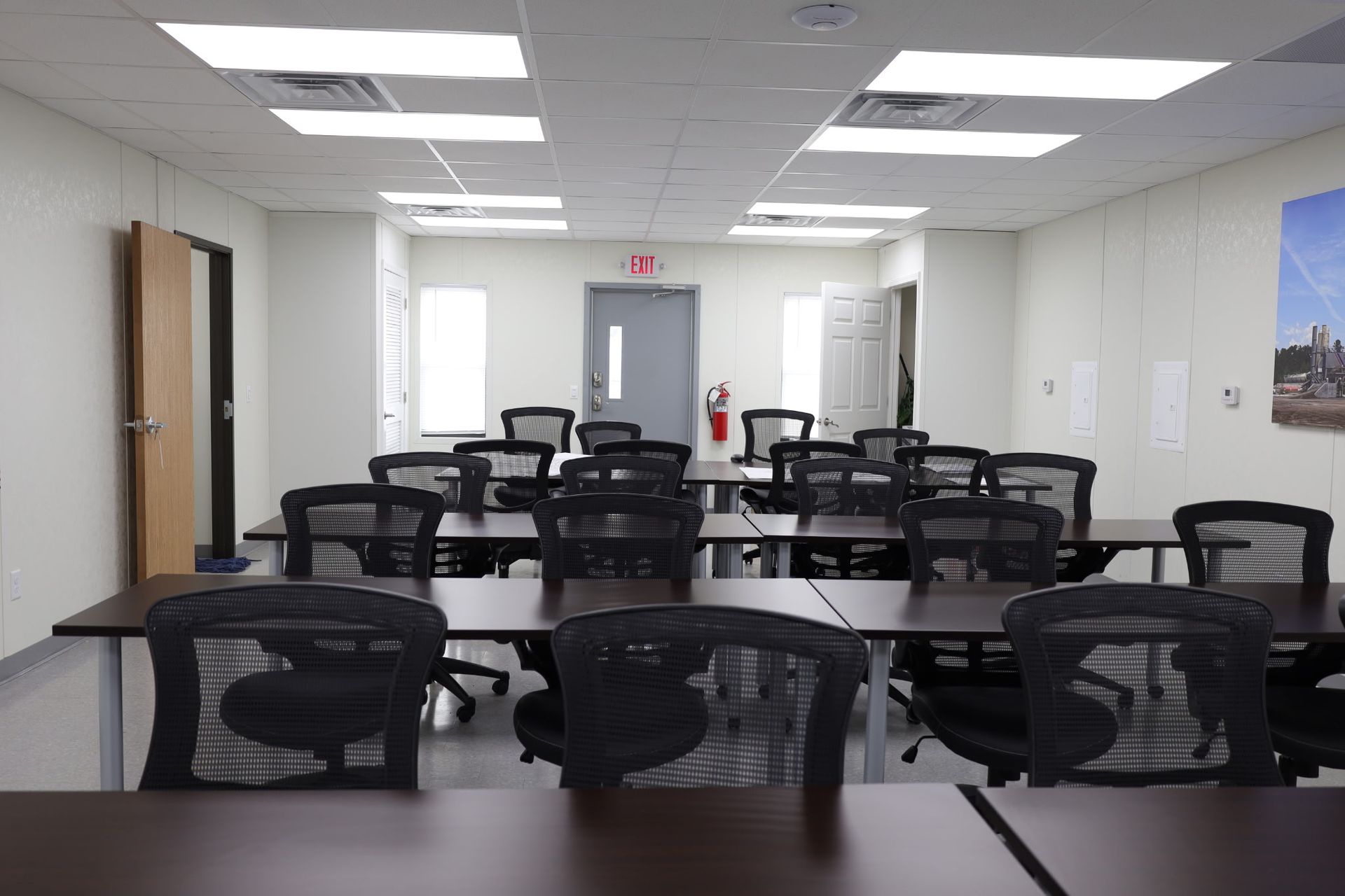 Empty classroom with rows of desks and chairs; emergency exit sign overhead.