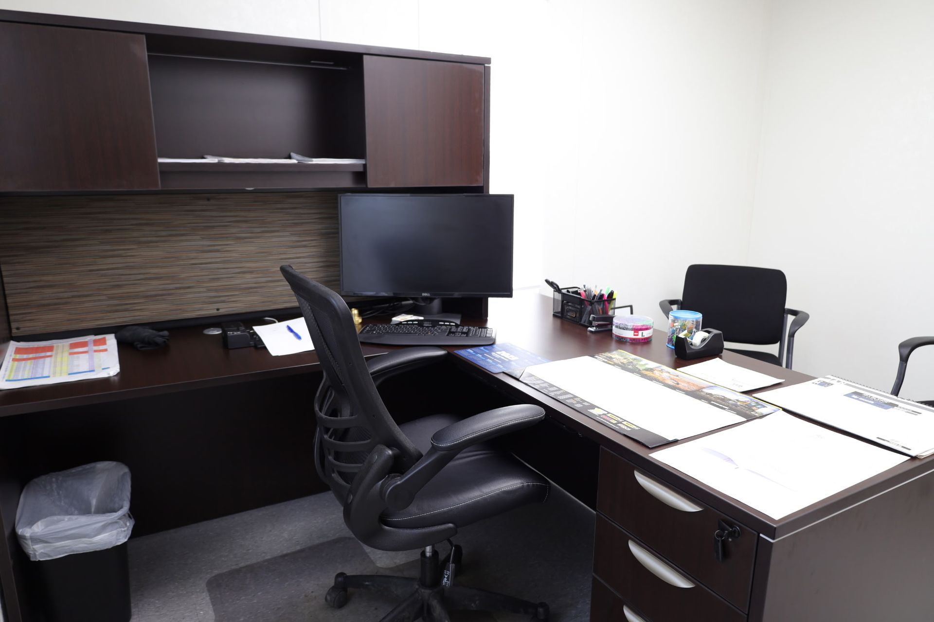 Office with desk, computer, chair, and cabinets. Brown and black furniture, white walls.