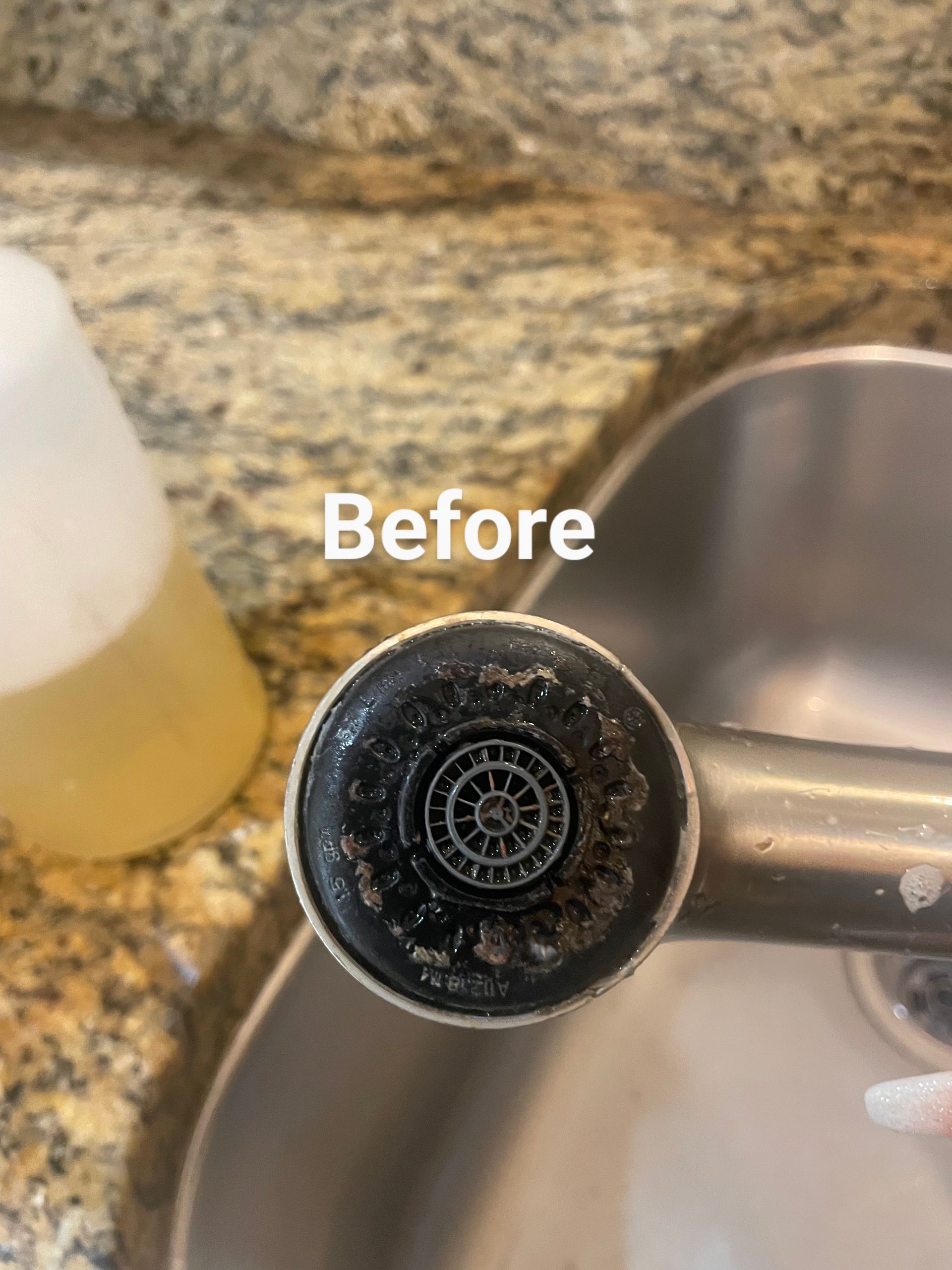 Close-up of a dirty kitchen faucet sprayer head covered in mineral deposits. The sink and counter are visible.