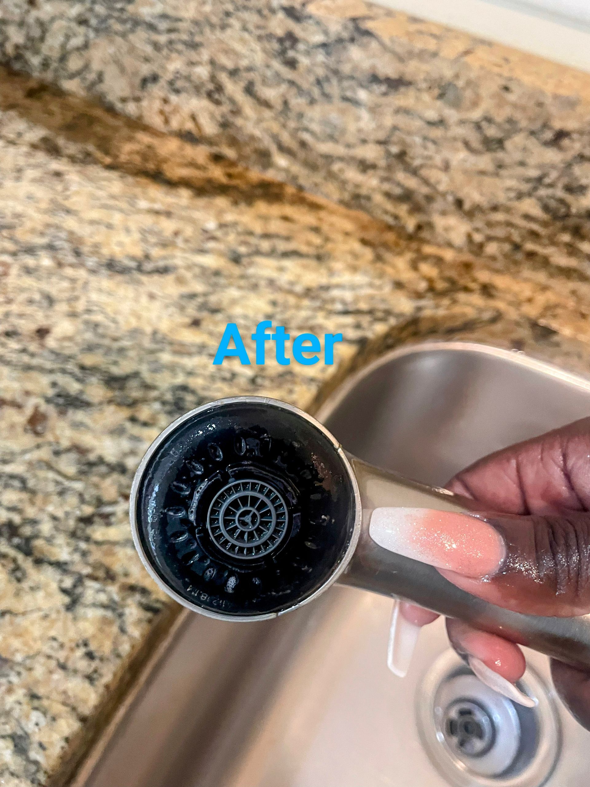 Hand holding clean faucet head over stainless steel sink, countertop in background, 