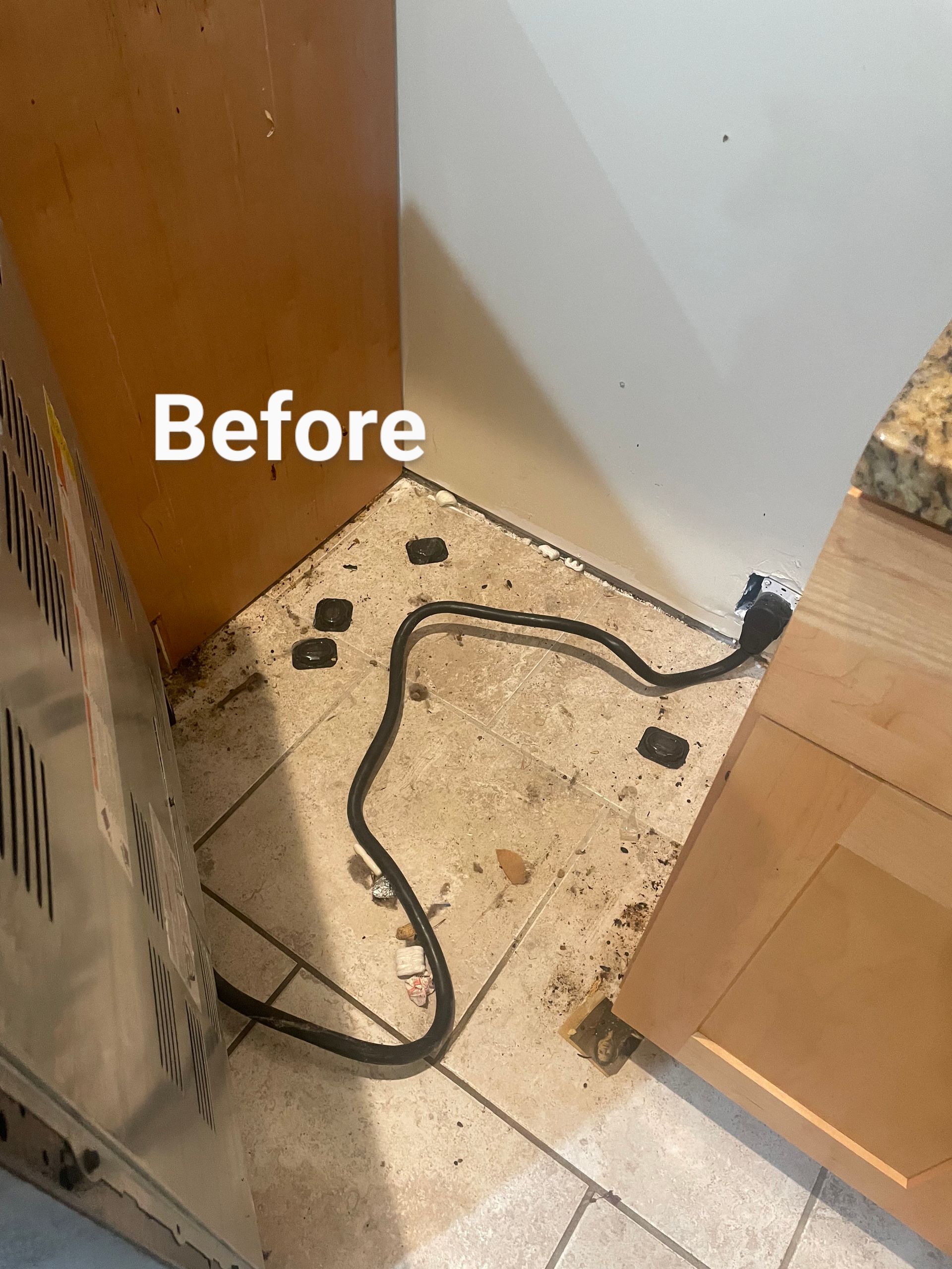 Dirty kitchen corner with debris on the floor, power cord, and tan cabinets.
