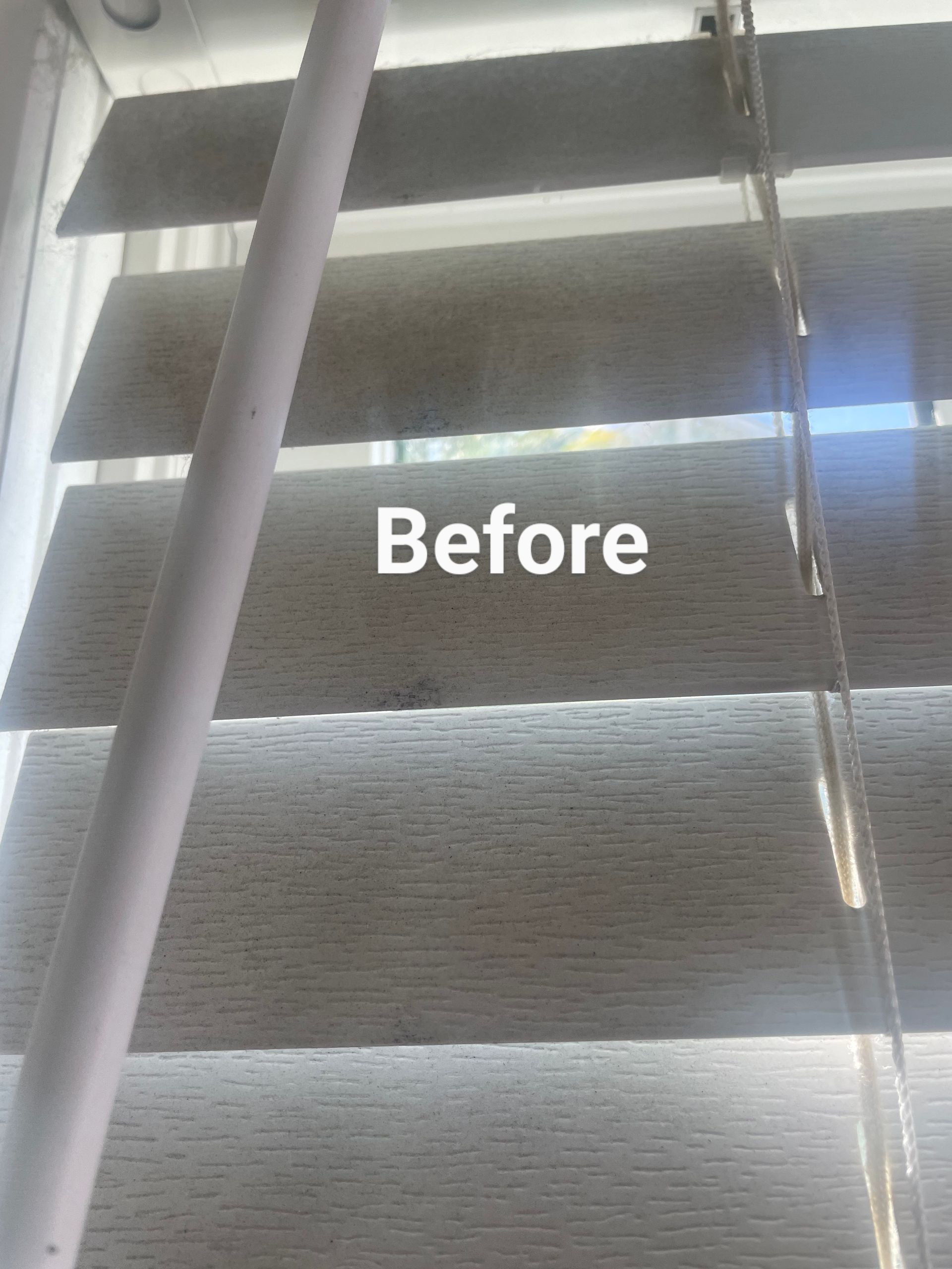 Close-up of a window with horizontal blinds partially open. A white vertical rod and cords are visible.