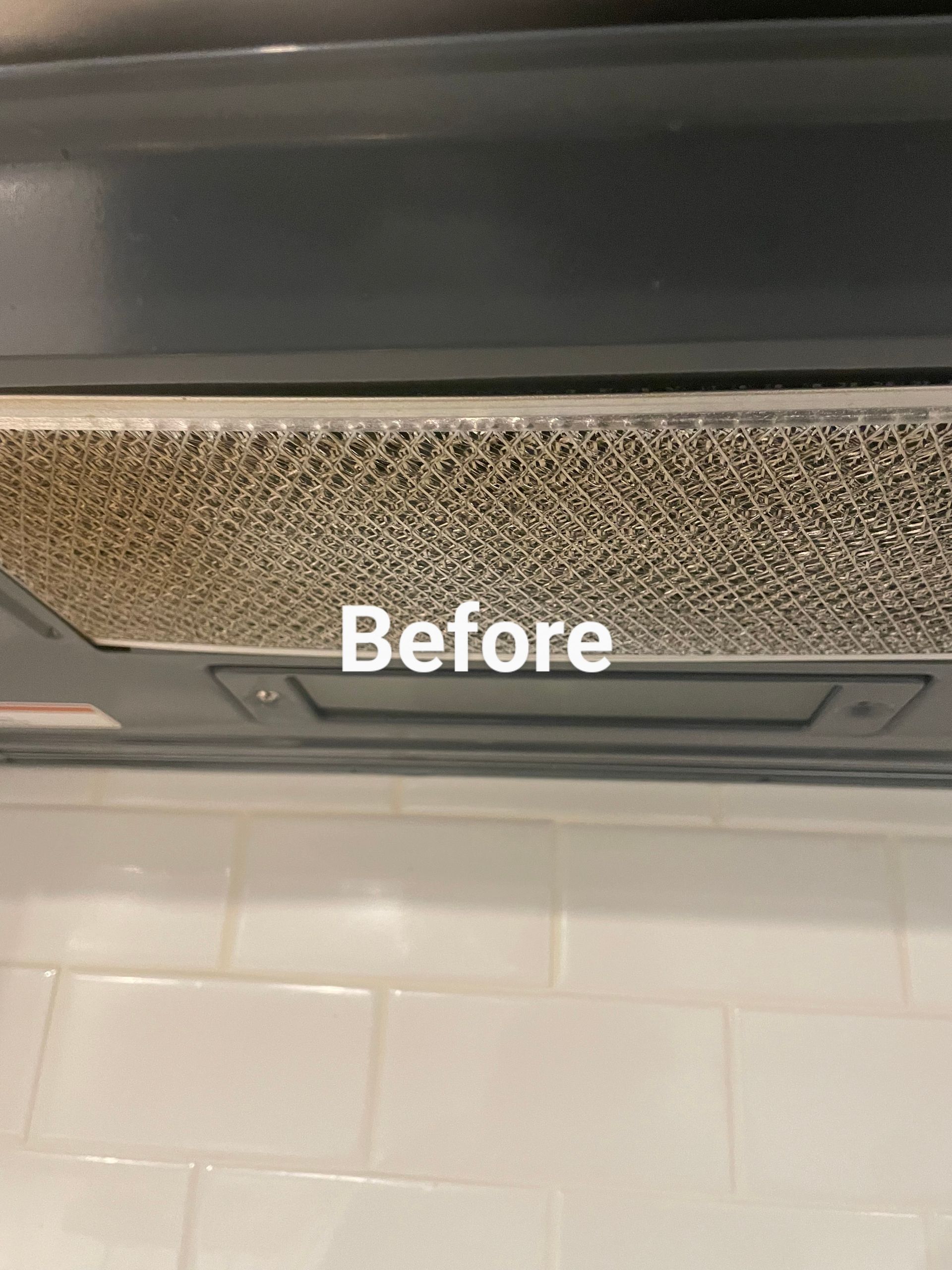 Dirty range hood filter above white tile backsplash.