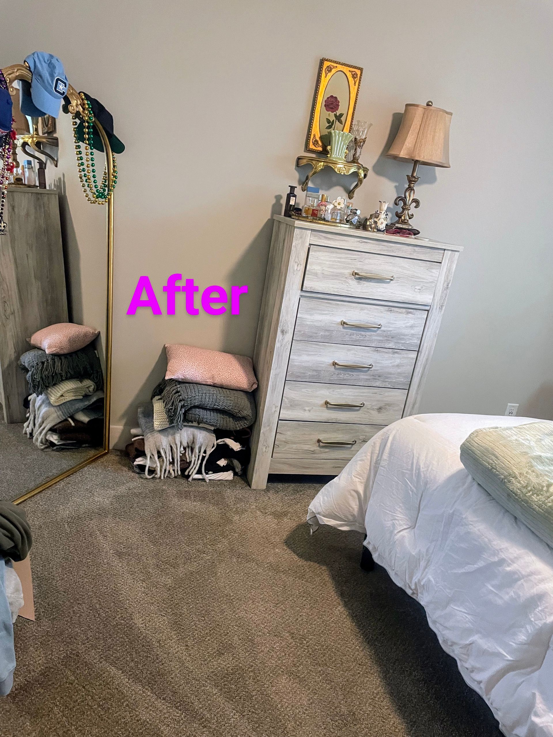 A bedroom corner with a dresser, a floor mirror, clothes, and a bed. 