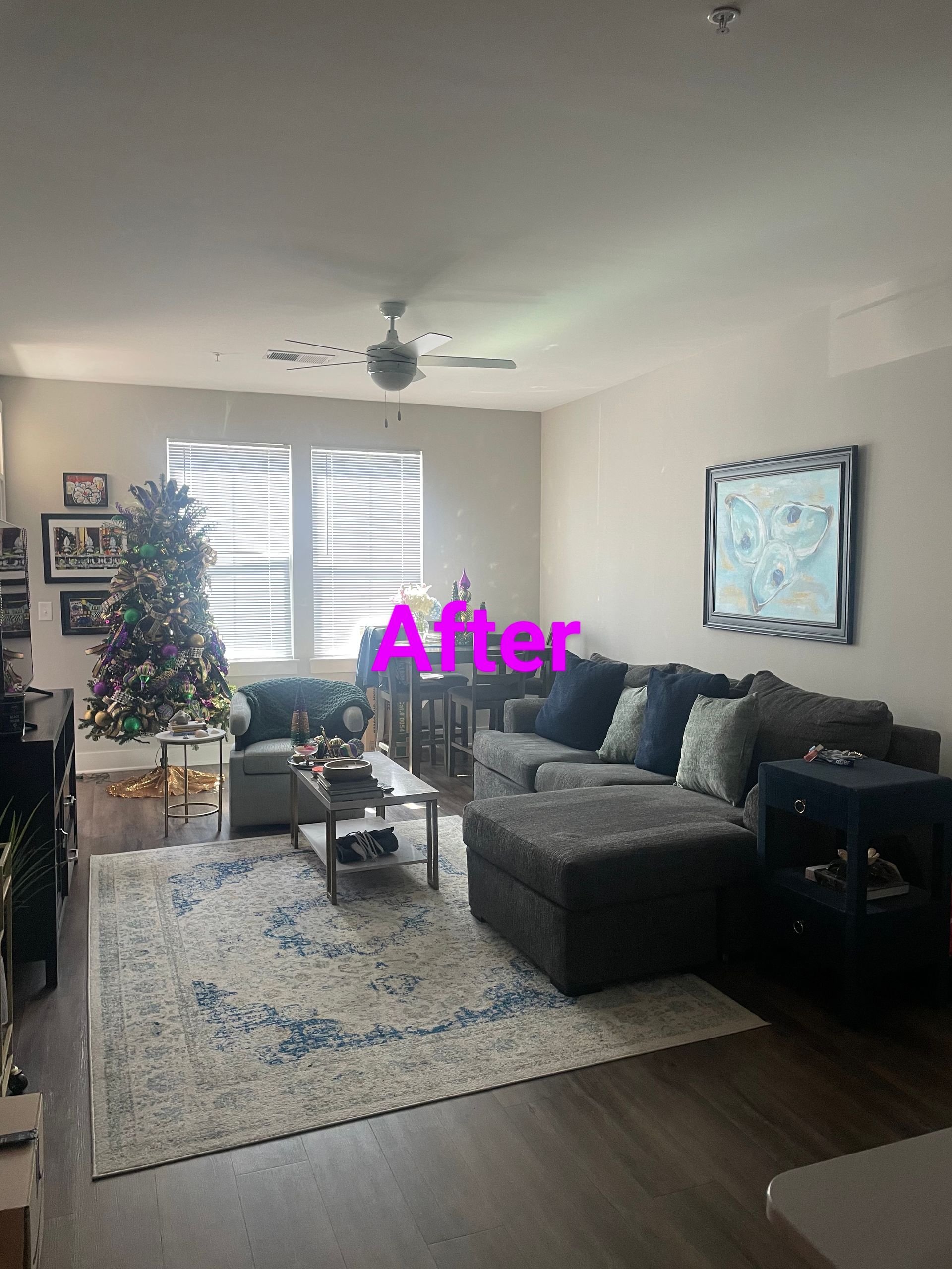 Living room with a dark gray sectional, rug, Christmas tree, and artwork. 