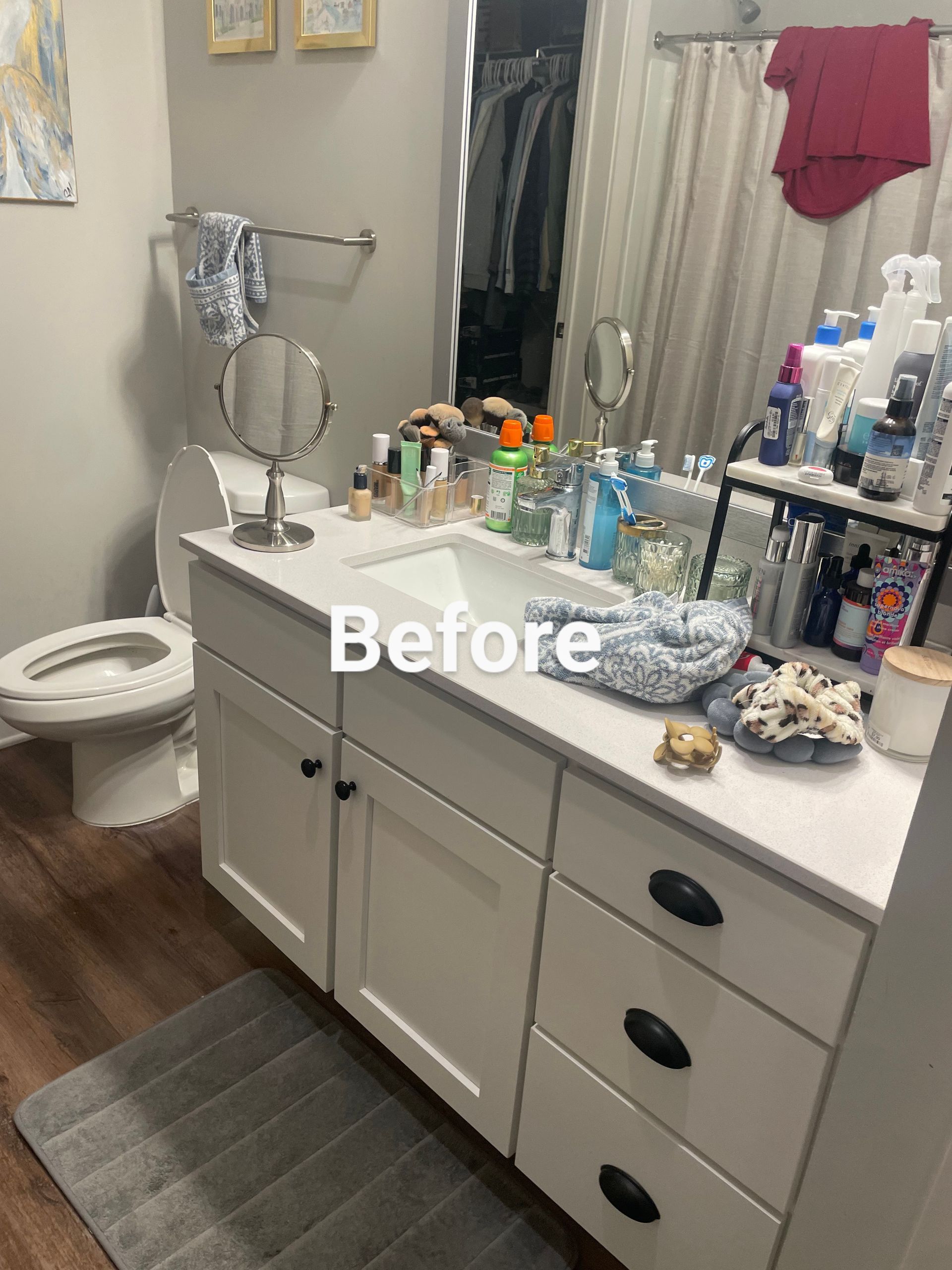 Cluttered bathroom with white vanity, toilet, and mirror.  Cosmetics and toiletries fill counter.