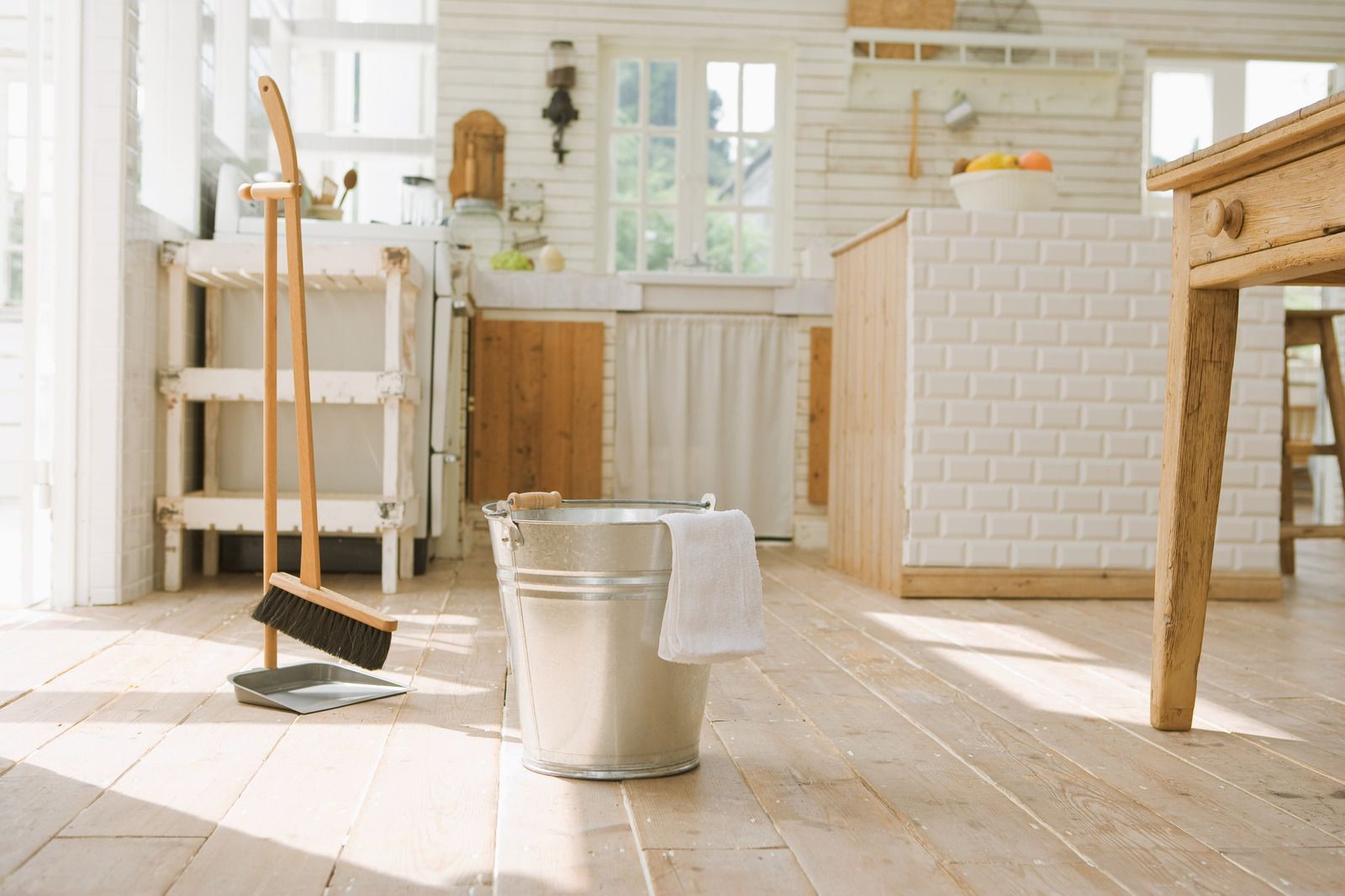 Cleaning supplies in a sunlit kitchen with a mop, bucket, and chair on a wooden floor.