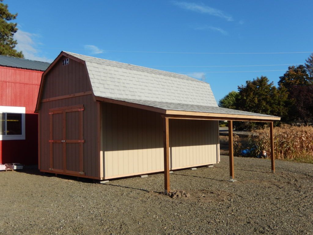 A barn with a carport attached to it is next to a red barn.