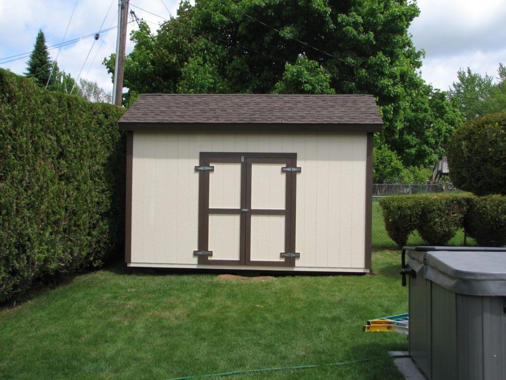A white and brown shed with a hot tub in the background