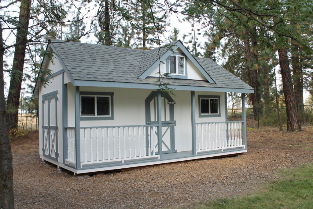 A small white house with a porch and trees in the background