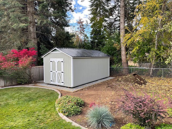 A small white shed is sitting in the middle of a lush green yard.