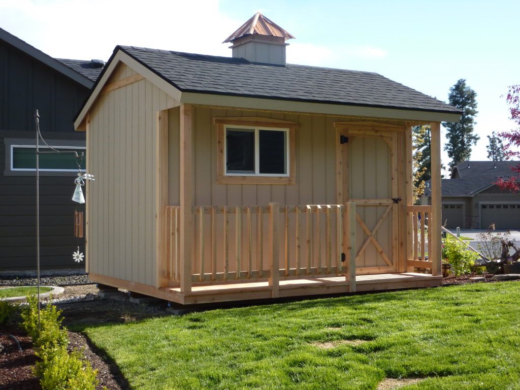 A small wooden shed with a porch in front of a house.