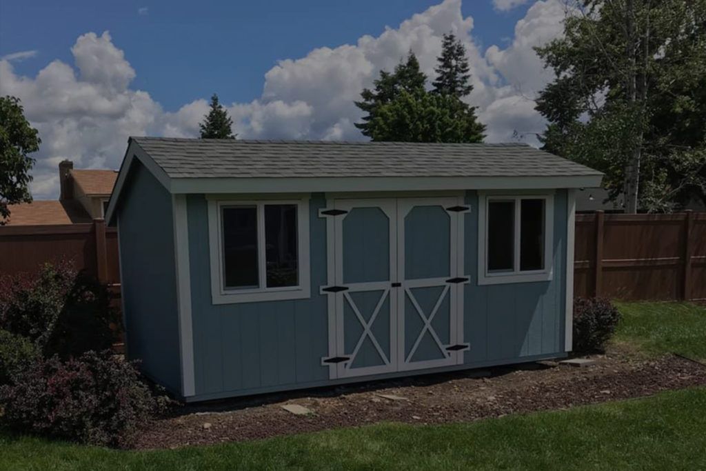 A blue shed is sitting in the middle of a lush green yard.