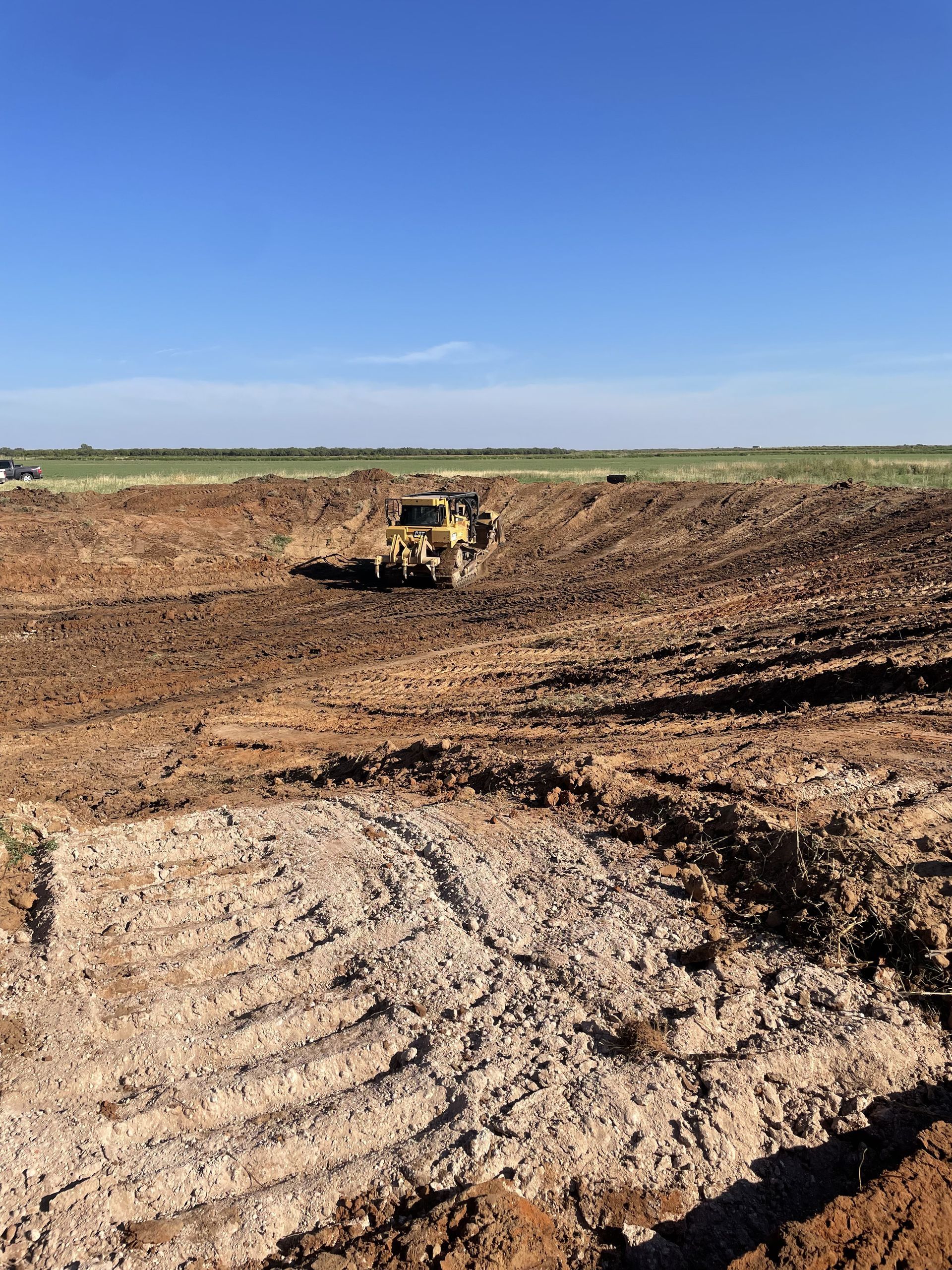 A bulldozer in a large, muddy excavation under a bright blue sky.