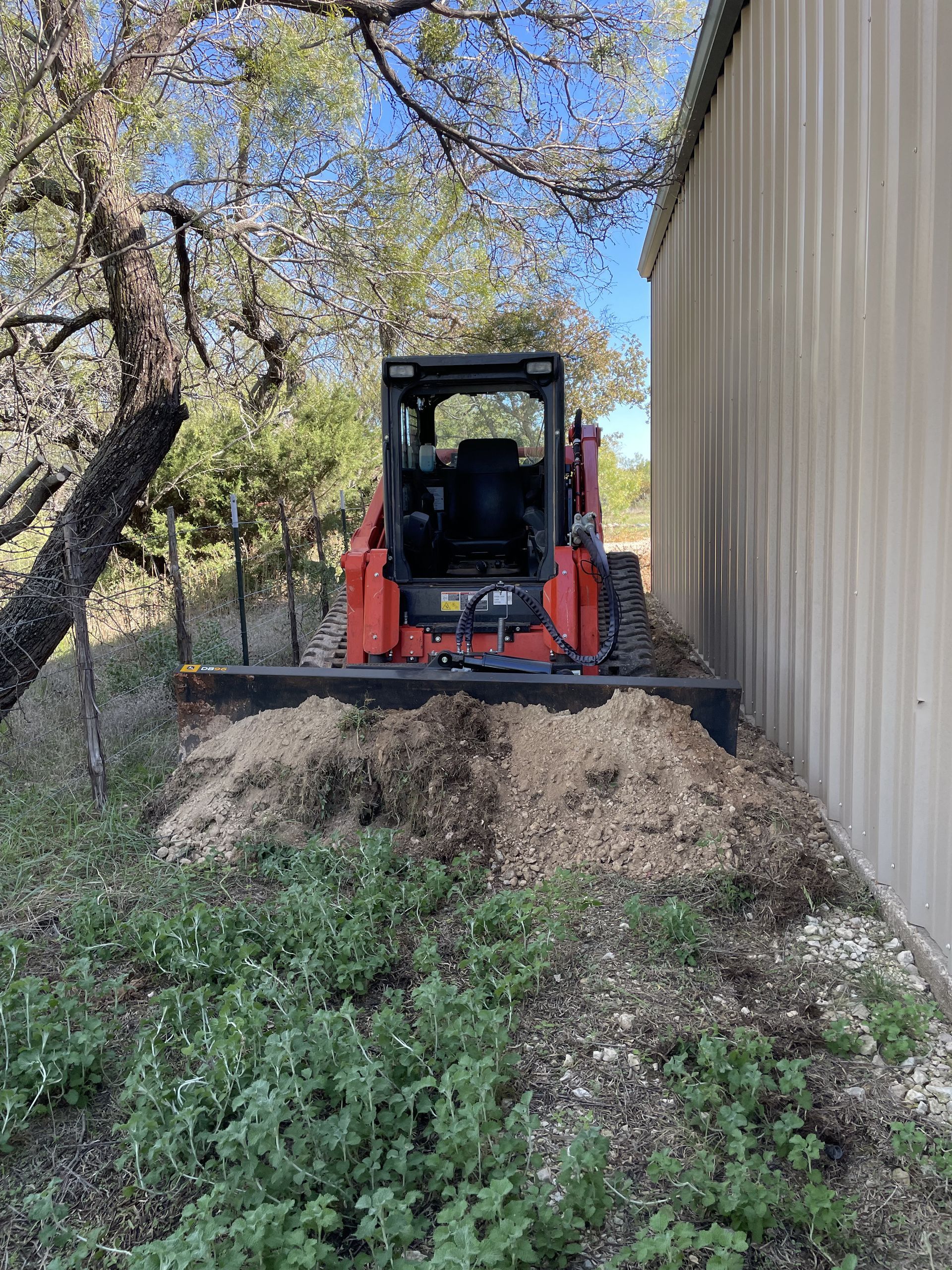 Orange skid steer with a blade clearing debris next to a building.