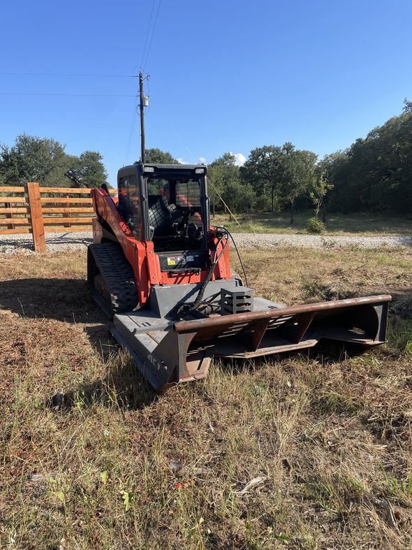 Orange and black tracked skid steer with a brush cutter attachment in a field.