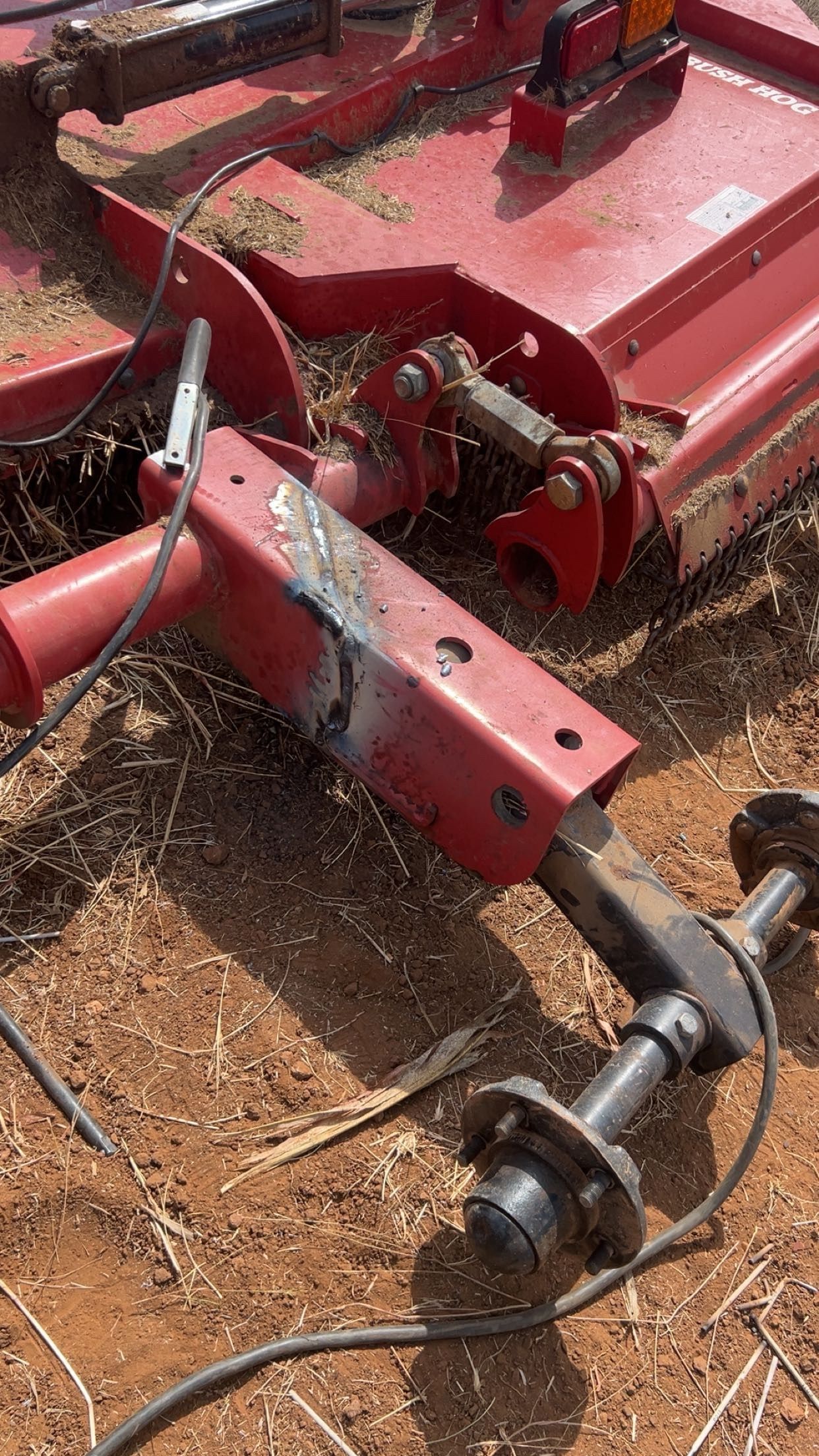 Red brush hog with welded repairs, outdoor setting.