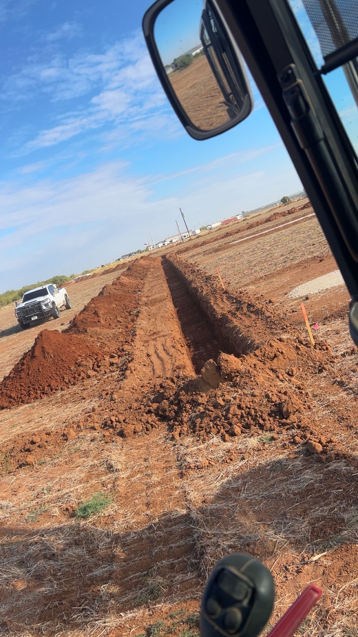 A tractor digging a trench in a field under a blue sky, a truck visible in the distance.
