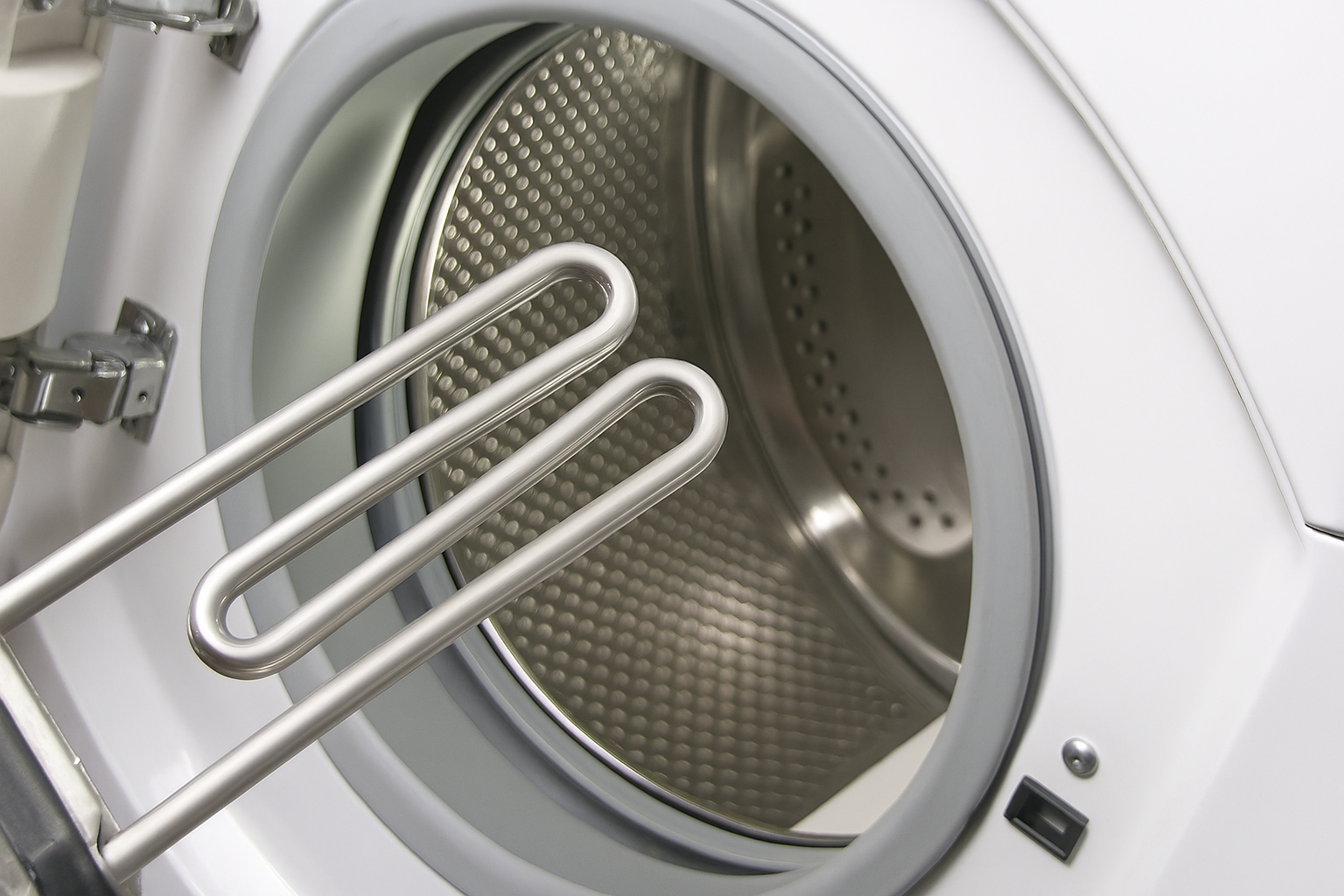 Interior de la lavadora con resistencia extendida dentro del tambor. Electrodoméstico blanco, interior metálico.