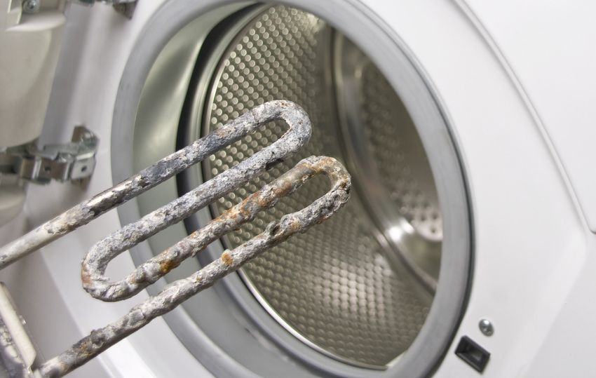 Primer plano del interior de una lavadora con dos resistencias muy corroídas extraídas.