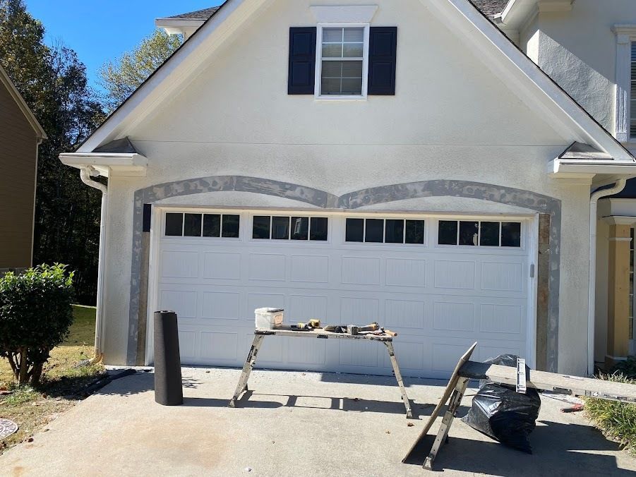 White garage door on house with gray trim; painting supplies on a work table, sunny day.