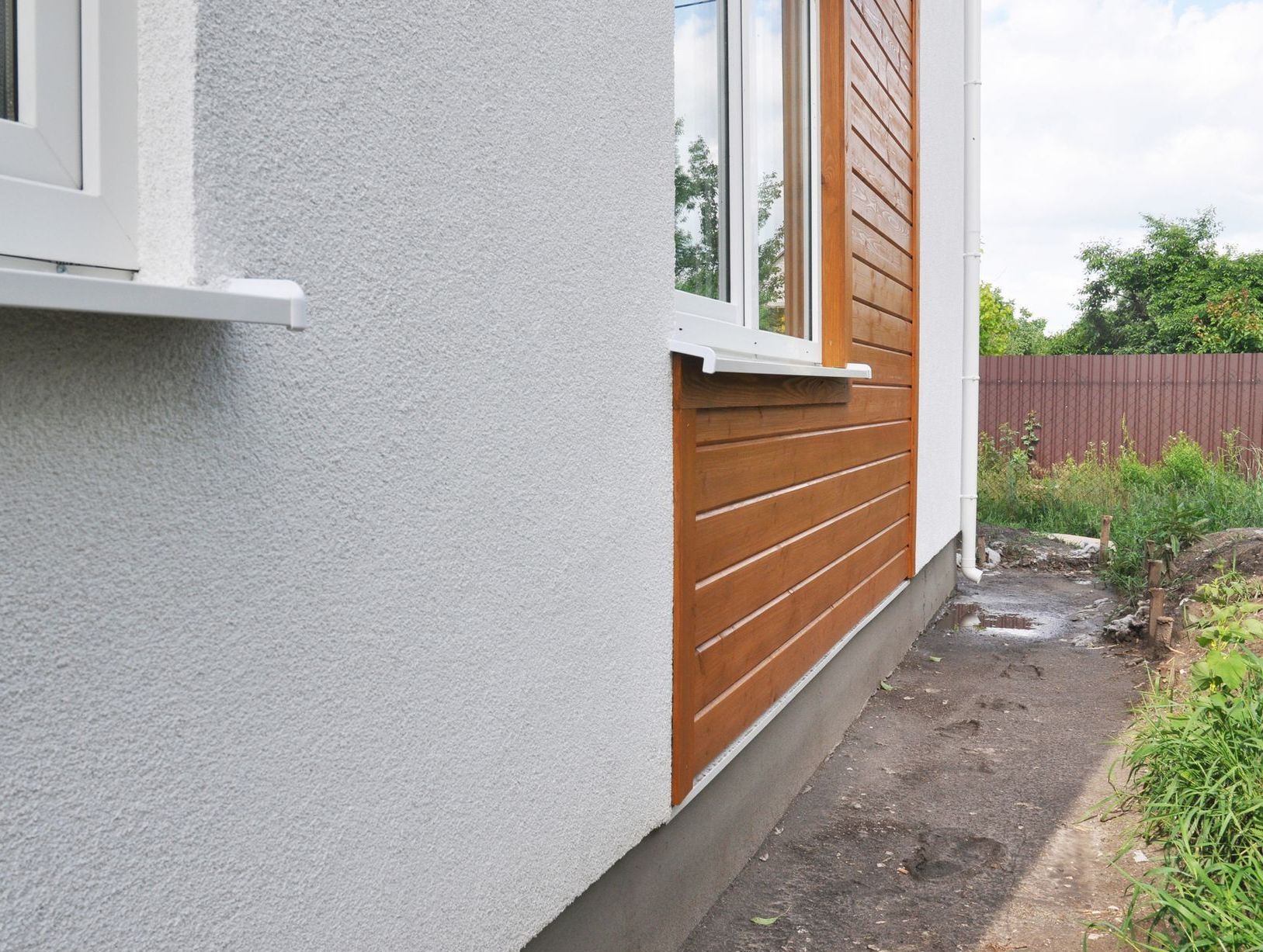 Exterior wall of a house, with textured white stucco and brown horizontal siding near a window.