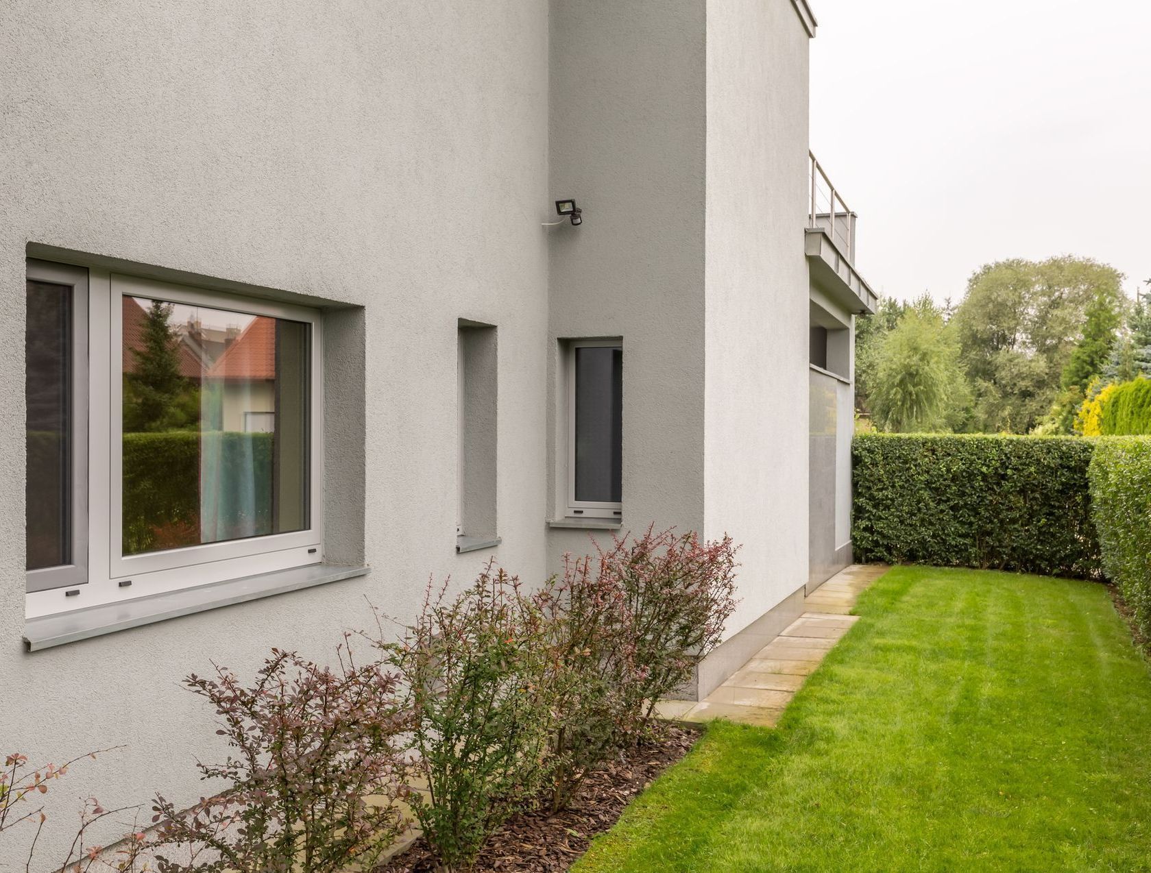 Exterior of a modern gray house with a window and small bushes next to a green lawn.