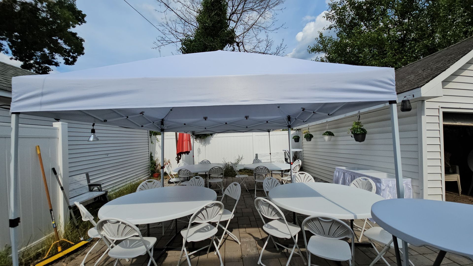 Outdoor event space under a white canopy with round tables and white chairs, set up on a patio.