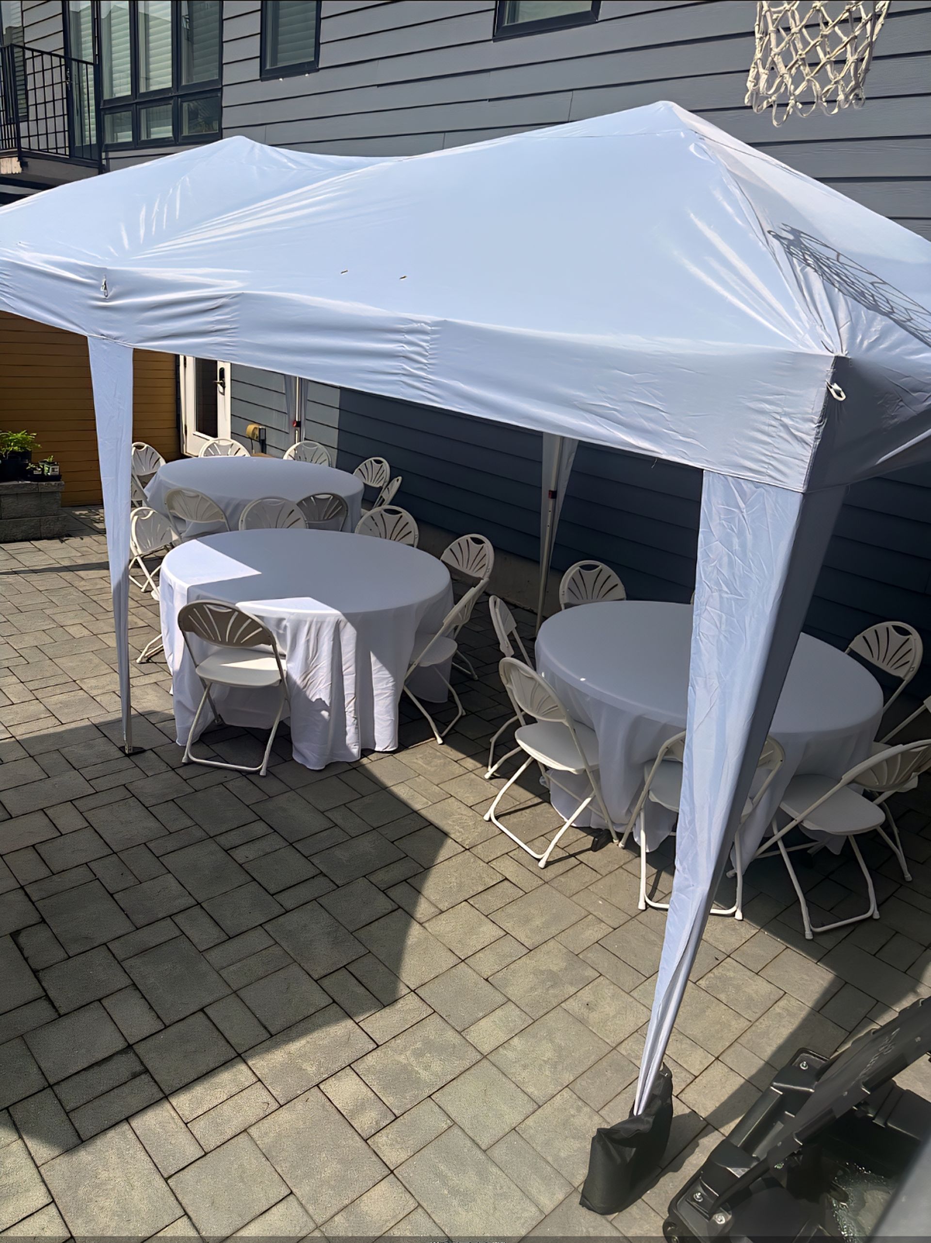 White tent over round tables and chairs set up on a patio. The tables are covered with white tablecloths.