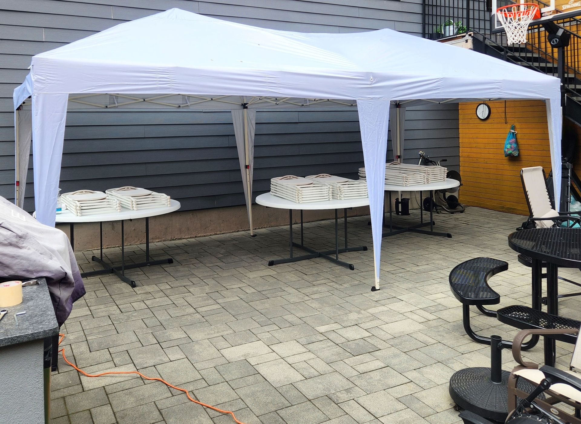 White canopy over outdoor tables set up on a patio; a few tables hold covered food items.