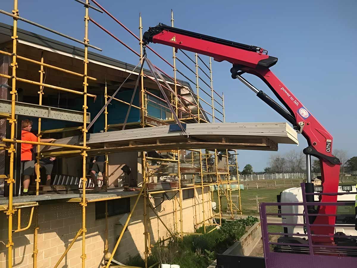 A Red Crane Is Lifting A Piece Of Wood On Top Of A Building — Snap Crane Truck Hire in Coffs Harbour, NSW