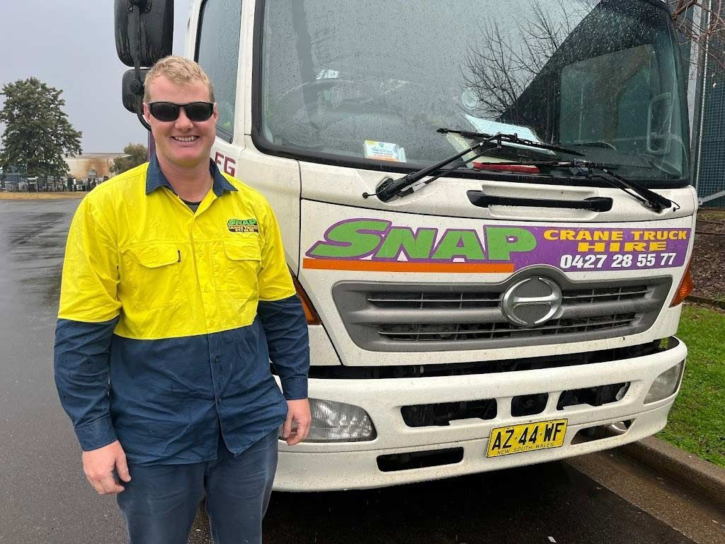 A Man In A Yellow Shirt Is Standing In Front Of A White Truck — Snap Crane Truck Hire in Coffs Harbour, NSW