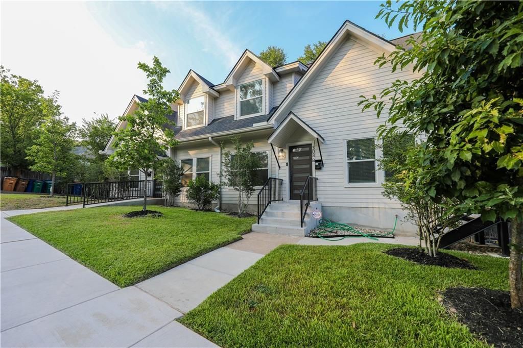 Gray house with white trim, green lawn, trees, and a concrete path.