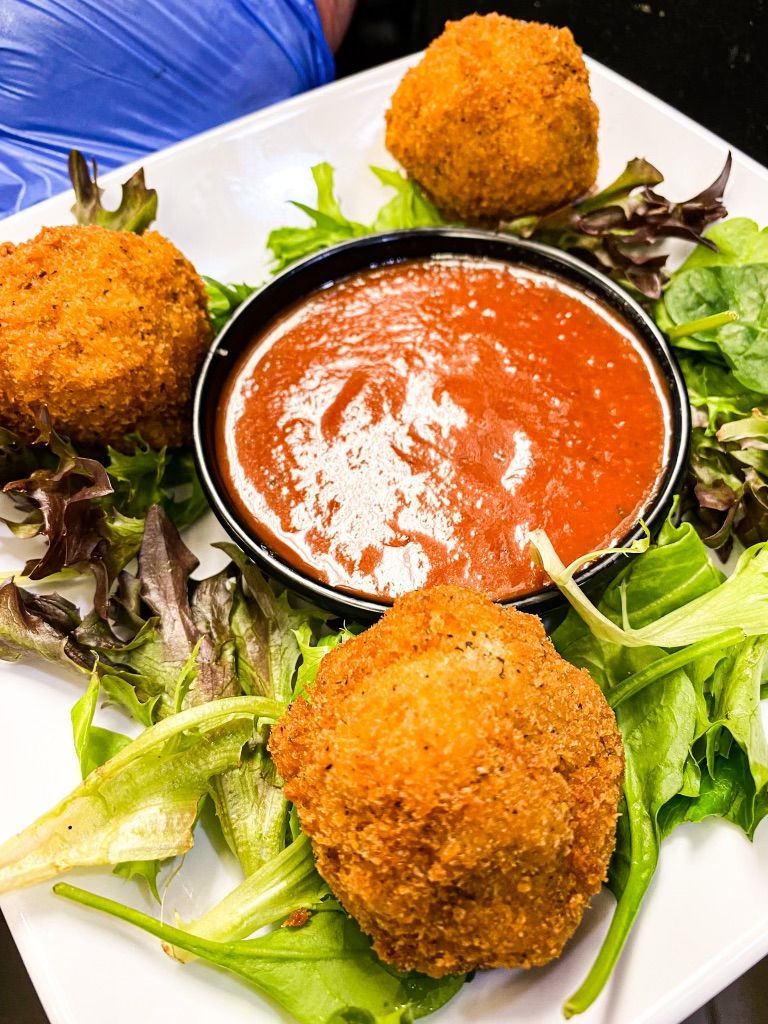 Three fried, golden-brown arancini balls served on a bed of fresh mixed greens with a side of marinara sauce.