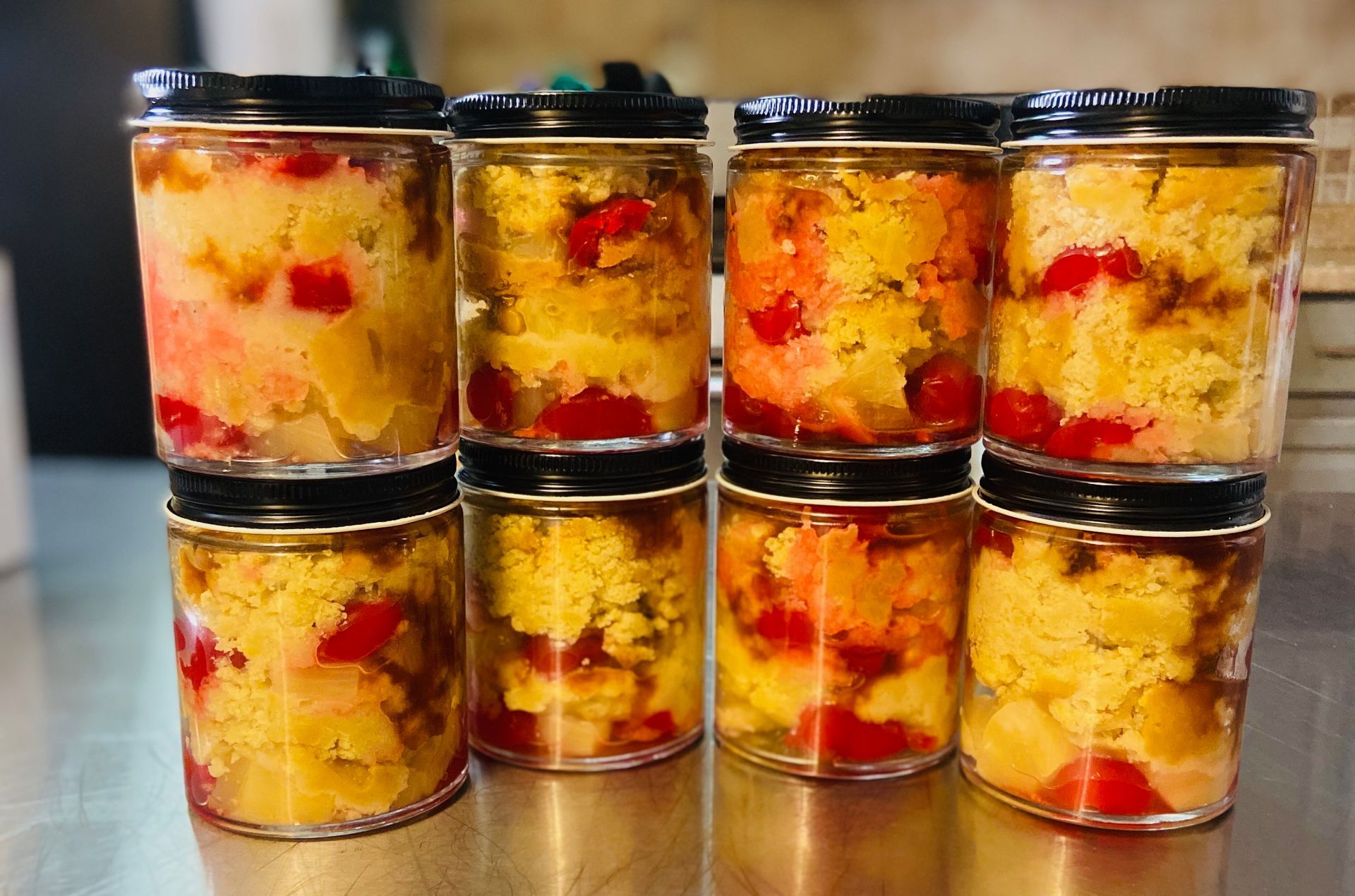 Eight glass jars filled with pineapple upside-down cake, arranged in two rows on a stainless steel surface.