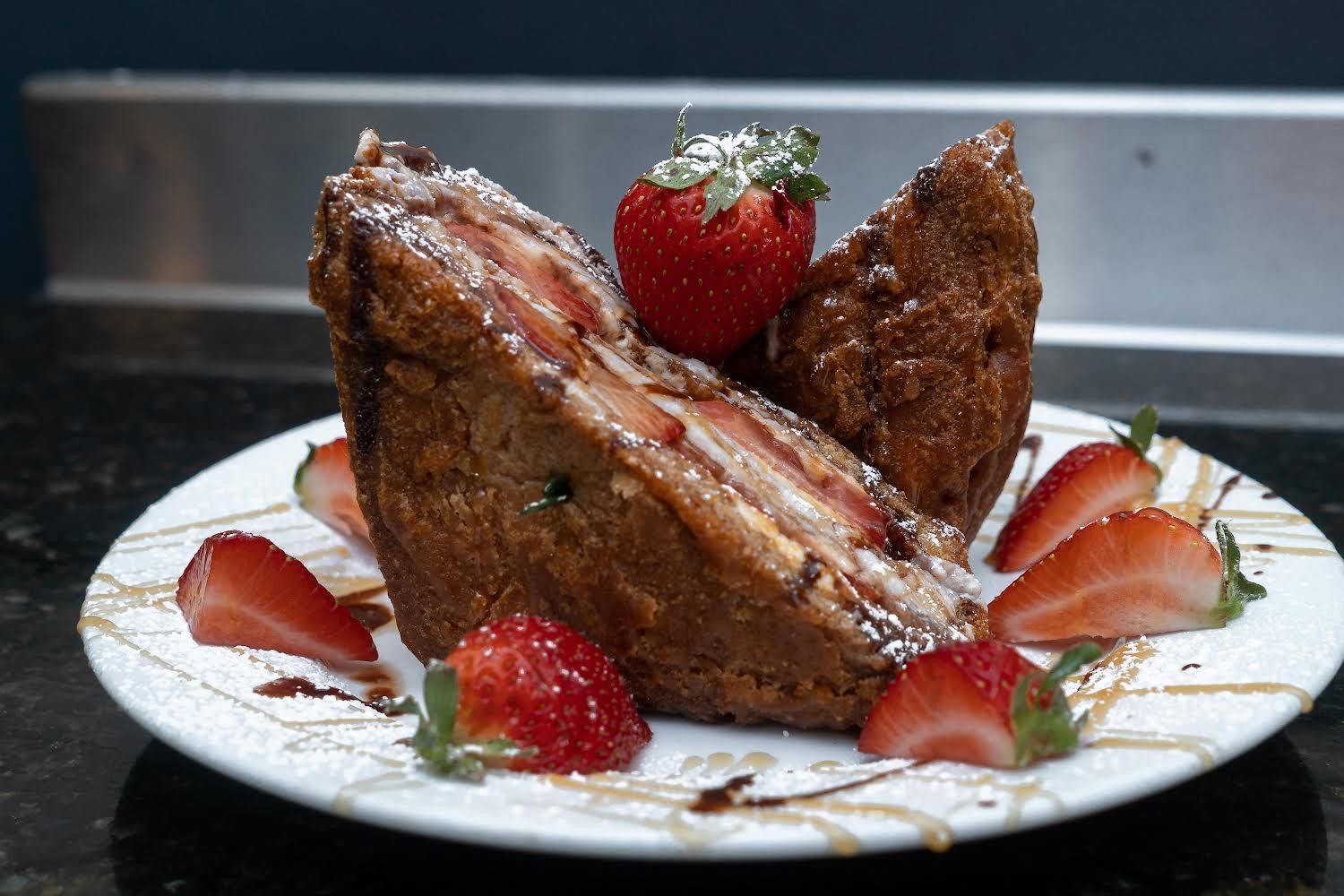 A plate with two pieces of thick, golden-brown stuffed French toast topped with fresh strawberries and powdered sugar.