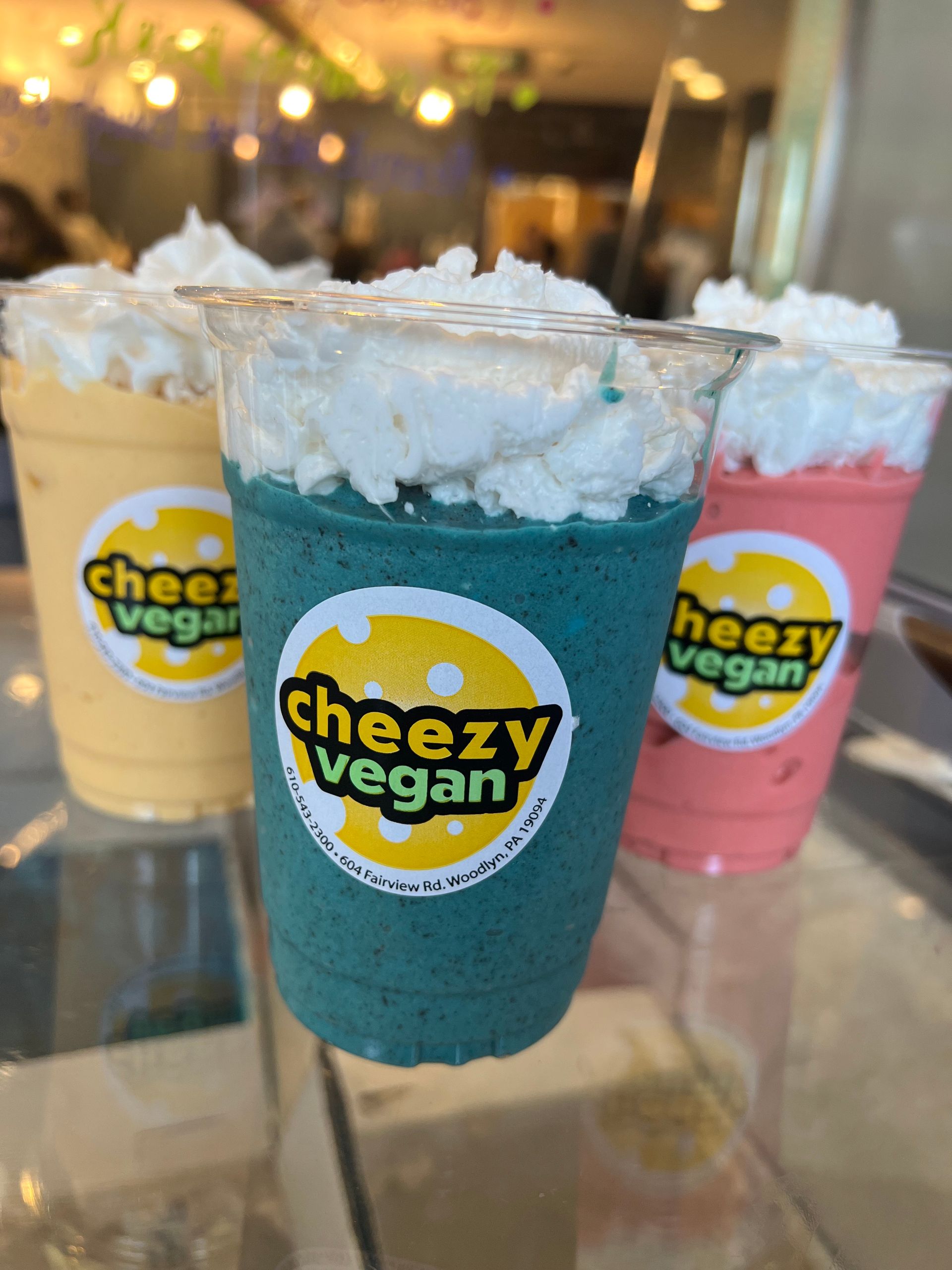 Three smoothie cups in yellow, blue, and pink, topped with whipped cream and featuring