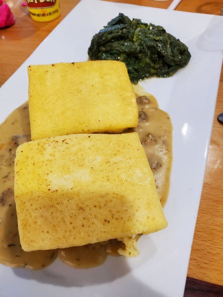 Two golden polenta cakes with gravy and spinach on a white plate.
