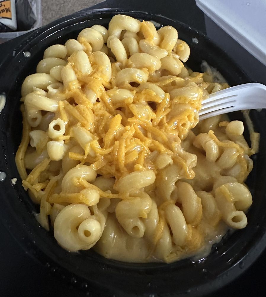 Mac and cheese in a black bowl, with a white fork. Yellow noodles and cheese.